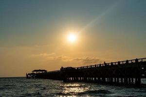 silueta del muelle del puente. el sol está cayendo en el mar de andaman. playa de natai en phang nga, tailandia foto