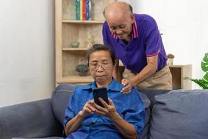 Asian senior holding mobile smart phone communication online internet video call together on sofa at home. photo