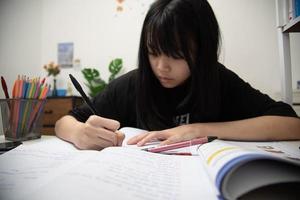 una estudiante asiática está escribiendo deberes y leyendo un libro en el escritorio foto
