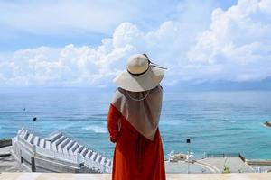 Portrait back of muslim woman wearing dress, hat and hijab in front of the beach photo