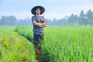 Attractive cheerful young Asian farmer standing, smiling and confident showing success to growing paddy rice in the rice field. Modern agriculture concept. photo