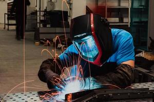 Professional Heavy Industry Welder Working Inside factory, Wears Helmet and Starts Welding. Selective Focus photo