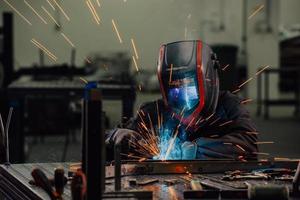 Professional Heavy Industry Welder Working Inside factory, Wears Helmet and Starts Welding. Selective Focus photo