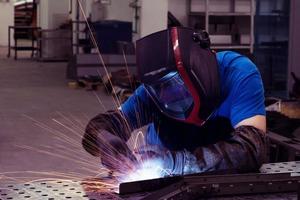 Professional Heavy Industry Welder Working Inside factory, Wears Helmet and Starts Welding. Selective Focus photo