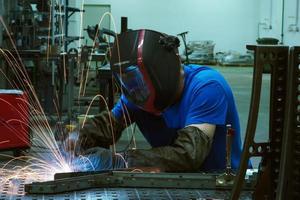 Professional Heavy Industry Welder Working Inside factory, Wears Helmet and Starts Welding. Selective Focus photo