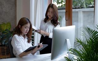Two young beautiful asian business woman in the conversation, exchanging ideas at work. photo