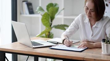 Serious focused Asian older 40s businesswoman executive manager sitting at desk working typing on pc laptop computer in contemporary office. Business online technology concept. photo