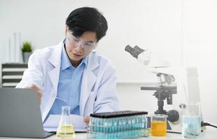 retrato de laboratorio de investigación médica de un apuesto científico masculino que usa una tableta digital, analizando bioquímicos líquidos en un matraz de laboratorio. foto