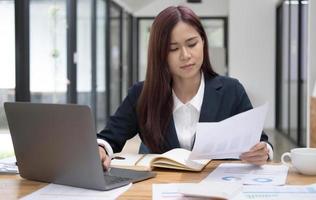 Confused asian businesswoman having a problem on her work or internet problem on laptop computer. Mistake, problem, or unsure with the project. photo