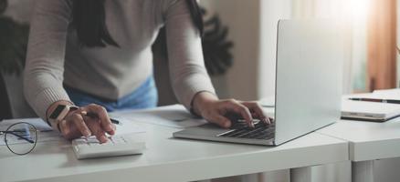 concepto de finanzas la mujer sostiene un bolígrafo gráfico, presiona una calculadora y gana dinero escribiendo informes y memorandos, y analizando documentos comerciales con una computadora portátil verticalmente. foto