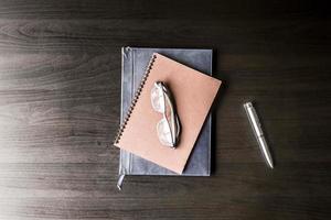 Top view of  notebook with glasses and pen on the black desk. photo