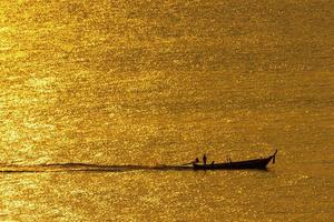 la puesta de sol, la superficie del mar refleja la luz del sol en oro. el barco atravesó la brillante superficie del mar. foto