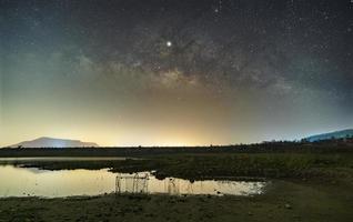 las estrellas en el cielo reflejan la luz de la noche. la vía láctea sobre las montañas y el estanque mae prachan represa y embalse, phetchaburi, tailandia foto