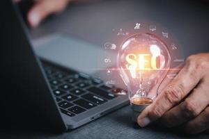 Marketer hold a light bulb showing SEO concepts, optimization analytics tools, search engine rankings, social media sites based on results analytics data. Customers use keywords to connect products photo