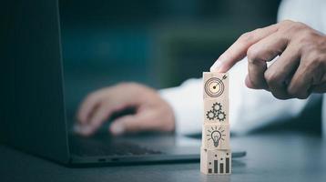 Businessman pointing at wooden blocks, goal setting ideas and business strategies. through planning and teamwork To analyze and develop company performance from growth data to the future. photo