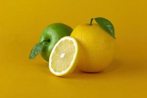 A green nature apple with yellow lemon fruits and a Lemon slice with leaf isolated on yellow background photo