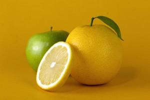 A green apple with lemon fruits and a Lemon slice with leaf isolated on yellow background, for concept of healthy fruit design photo