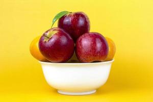Natural Healthy fruits in a white bowl, green apples, red apples, oranges isolated on yellow background. Creative composition of colorful of fruits isolated on yellow background photo