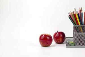 Education elements in the box, color pencils, face mask, paper clips, scissors, ruler, two red apples isolated on white background. Back to school concept art photo