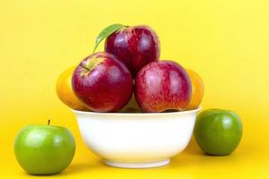 Set of Healthy fruits in a white bowl, green apples, red apples, oranges isolated on yellow background. Close up composition of colorful of fruits isolated on yellow background photo