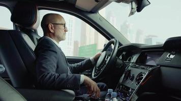 l'autista di una roll-royce in una business suite al volante, fa girare il controller sul pannello di controllo. sfondo, città, edifici, grattacieli video