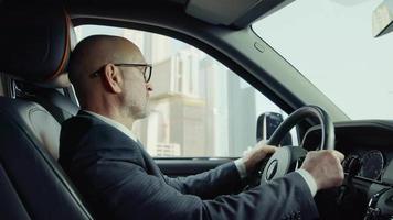 el conductor con traje, viaja tranquilamente en un rolls-royce. fondo ciudad edificios rascacielos video