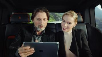 les passagers sont assis dans une rolls-royce, regardent une tablette et parlent, route de montagne video