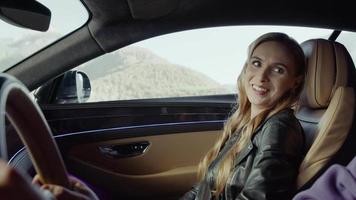 A girl passenger is sitting in a Bentley, laughing and looking at the driver, Trees flash against the background of the mountain