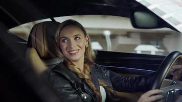 bentley.de bestuurder is een meisje dat een auto bestuurt en met een passagier praat. achtergrond,stad,gebouwen,wolkenkrabbers video