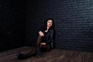 Studio portrait of sexy brunette girl in black leather jacket against brick wall. photo