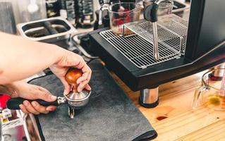 The barista presses ground coffee using a tamper on a wooden counter with an automatic coffee machine placed in the coffee shop. photo