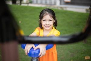 una chica feliz asiática con vestido naranja está jugando en el patio de recreo. foto