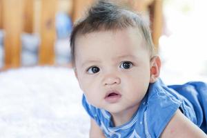 un hermoso bebé de 6 meses con ojos grandes yace en la cama. foto