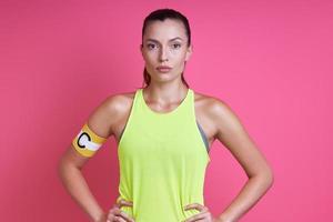 Confident woman in sports clothing wearing captain band and standing against pink background photo