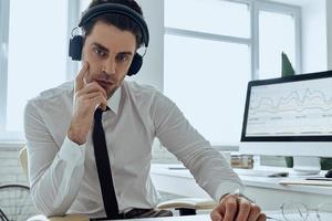 joven confiado en auriculares mirando a la cámara mientras está sentado en la oficina foto