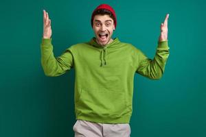 Excited young man gesturing while standing against green background photo