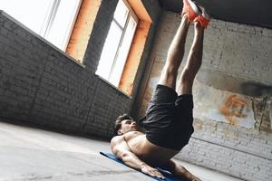 Confident young man keeping his feet up while training in gym photo