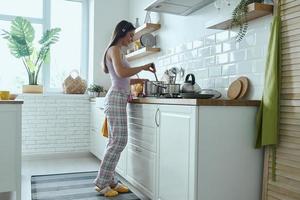 toda la longitud de una joven con auriculares disfrutando de la música mientras cocina en la cocina foto