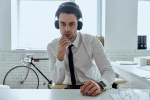 joven confiado en auriculares mirando a la cámara mientras está sentado en la oficina foto