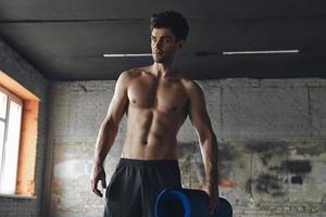 Handsome muscular man carrying exercise mat while standing in gym photo