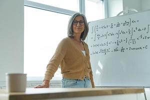 anciana enseñando matemáticas mientras está de pie cerca de la pizarra en el aula foto