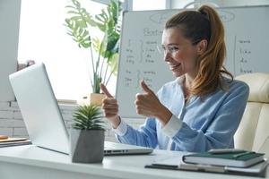 mujer feliz gesticulando mientras tiene una conferencia web cerca de la pizarra en el aula foto