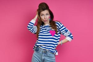 Playful young woman holding hand in hair while standing against colored background photo