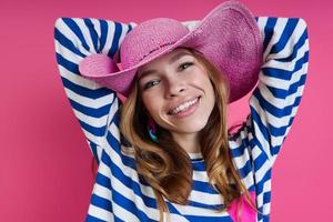 hermosa mujer con sombrero rosa tomándose de la mano detrás de la cabeza mientras se enfrenta a un fondo de color foto