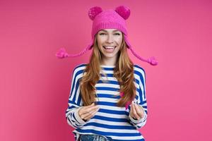 Una joven juguetona con sombrero rosa sonriendo mientras se enfrenta a un fondo de color foto