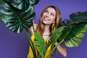 mujer joven atractiva mirando fuera de la planta y sonriendo mientras está de pie contra el fondo púrpura foto