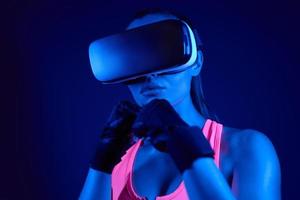 Young woman in virtual reality glasses standing in punching position against colorful background photo