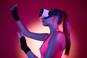 Young woman in virtual reality glasses gesturing against colorful background photo