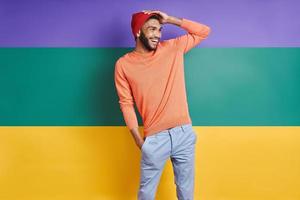 Handsome African man adjusting hat and smiling while standing against colorful background photo