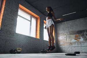 Full length of confident young woman jumping with rope in gym photo